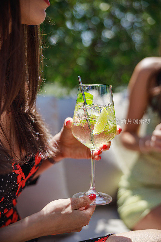 Woman holding a glass of cocktail on ice with stirring rod, outdoor café